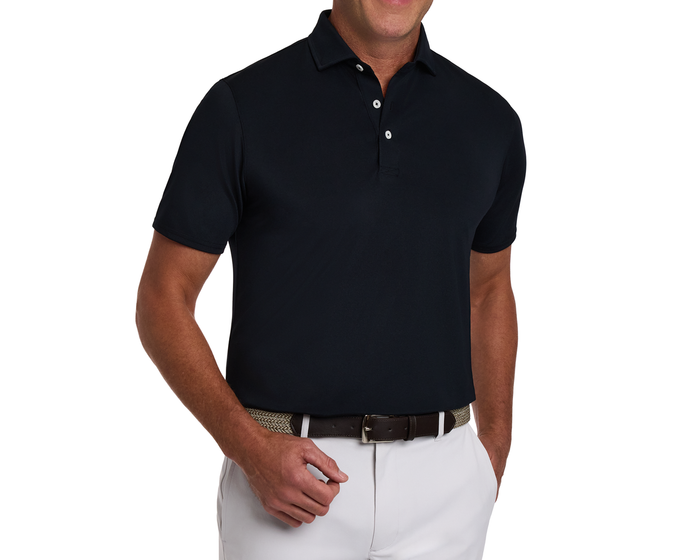 Man wearing The Macdonald Shirt: Black, a short-sleeve polo with contrast collar piping, tucked into light trousers, accessorized with a woven tan and brown belt.