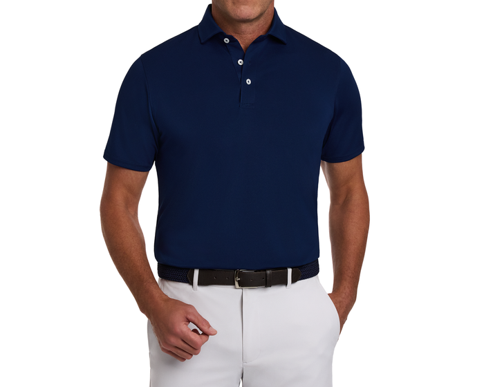 Man wearing The Macdonald Shirt: Navy, a modern polo with contrast collar piping, tucked into light trousers and paired with a dark braided belt.