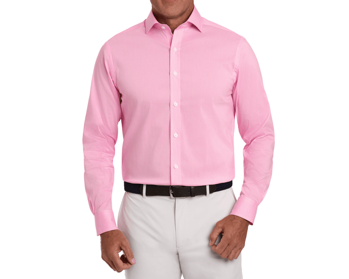 Man models The McAllister Shirt: Belmont, a light-pink, long-sleeve, button-down dress shirt, tucked into trousers with a dark woven belt.