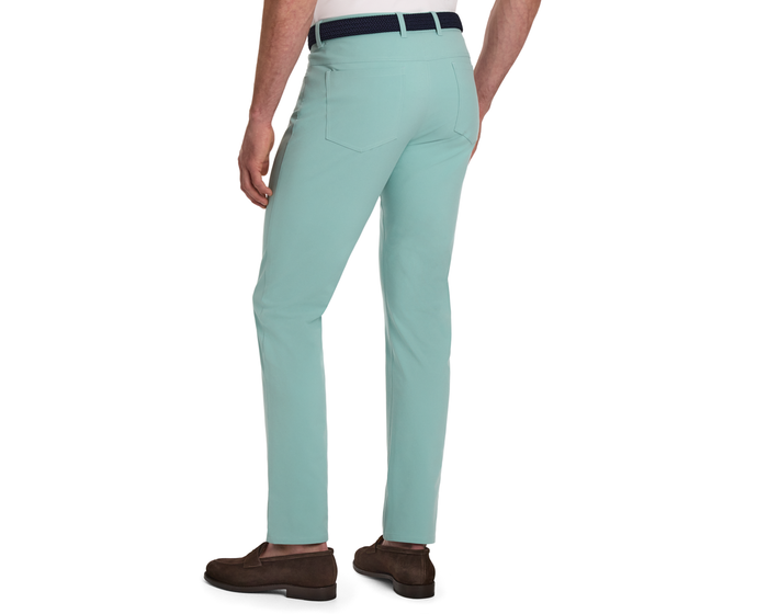 Rear view of a man wearing The McDaniel 5 Pocket Pant: Cascade Green, showcasing slim-fit trousers with a woven belt and brown suede loafers.