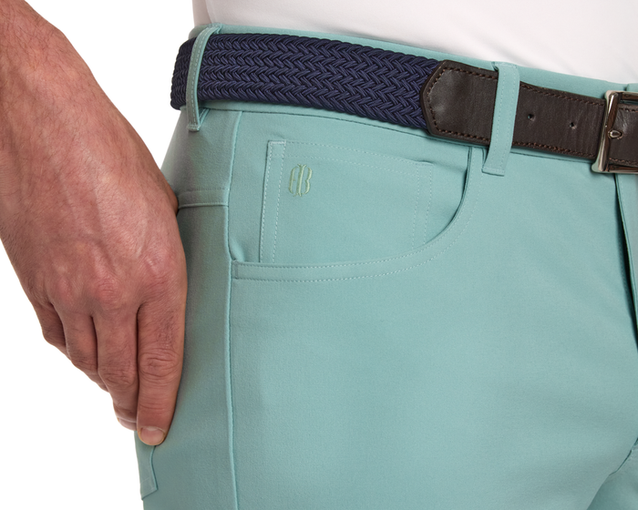 The McDaniel 5 Pocket Pant: Cascade Green, featuring a small logo and navy braided belt, showcases wrinkle-resistant, quick-dry performance fabric with eco-friendly stretch.