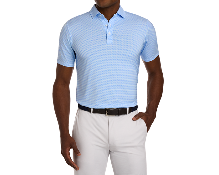 Model wearing The Norman Shirt: Vista Blue & Horizon Blue, a light-blue polo with geometric pattern, tucked into light trousers, highlighting its comfort and versatile style.