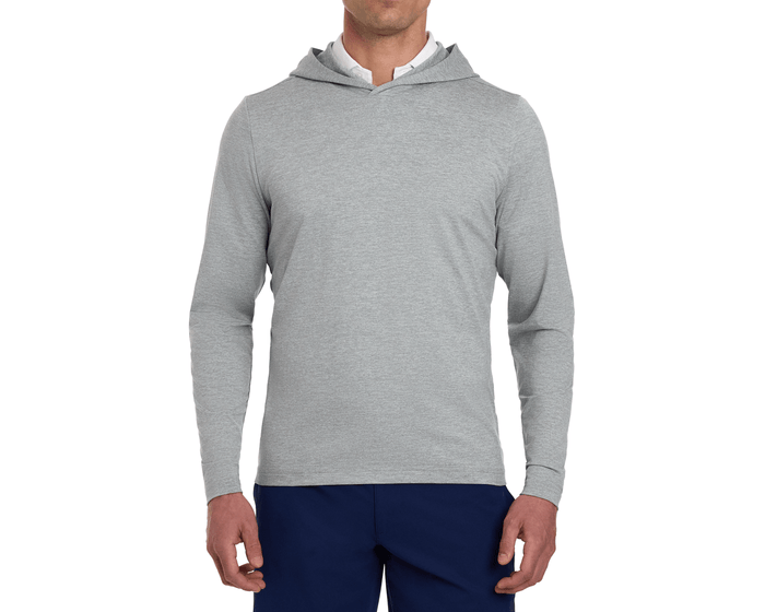 Male model wearing The Stowe Hoodie: Heathered Gray, featuring a light-gray long-sleeve design with set-in sleeves and an athletic drop-tail hem, paired with navy trousers.