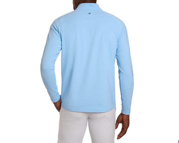 Model wearing The Stuart Quarter-Zip: Vista Blue, showcasing a light-blue, long-sleeve pullover with textured rib fabric, paired with light trousers against a plain background.