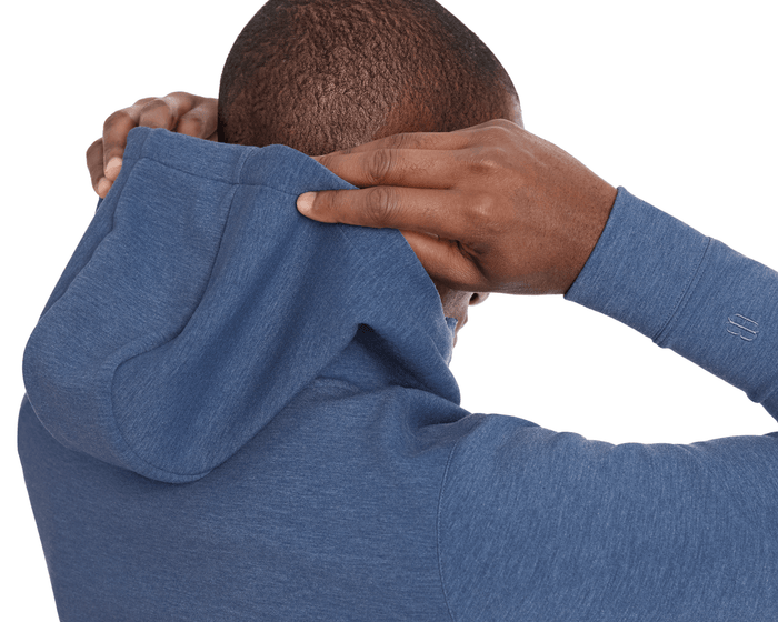 Person pulling up the hood of The Tilley Quarter-Zip Hoodie: Heathered Andover, showcasing its sleek silhouette and tonal embroidered logo on the sleeve.