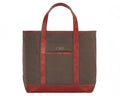 The Travis Tote Bag features brown canvas with reddish-brown leather trim, front pocket with CMB monogram, and is ideal for versatile use.