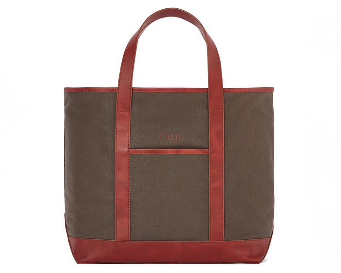 The Travis Tote Bag Cotton Twill features brown canvas with red leather trim, long handles, a front pocket, and CMB initials embroidered.