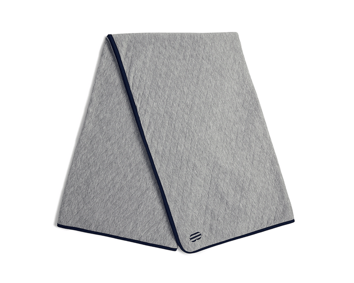 The Van Pelt Blanket: Heathered Gray, a light-grey quilted blanket with diamond stitching, dark-navy trim, and a minimalist logo embroidered near one corner.