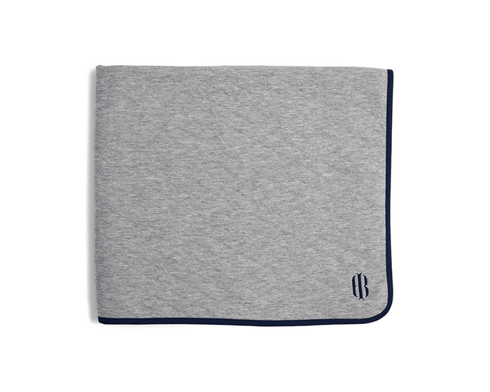 The Van Pelt Blanket: Heathered Gray with navy trim and embroidered logo, folded, showcasing its cozy, quilted fabric ideal for warmth and style.
