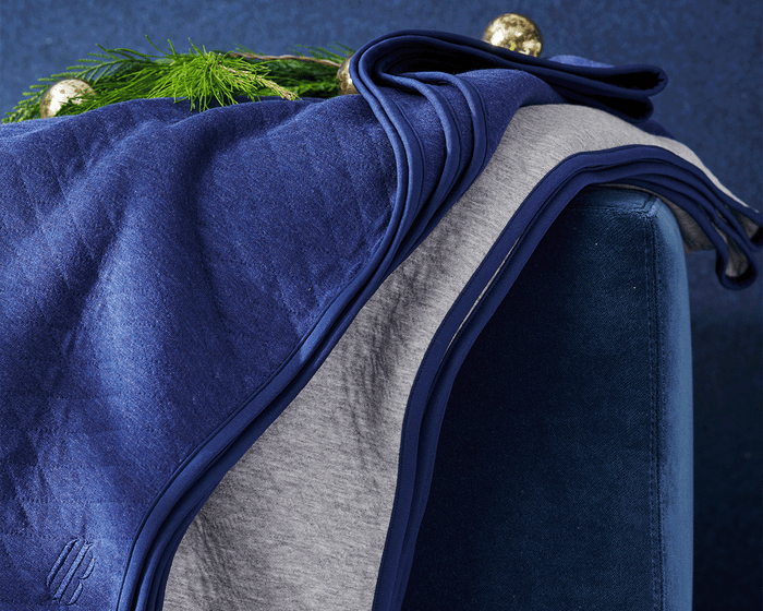 The Van Pelt Blanket: Heathered Gray, cozy and quilted, draped over a bench with holiday accents, ideal for cool evenings, featuring contrasting trim and H&B Icon logo.