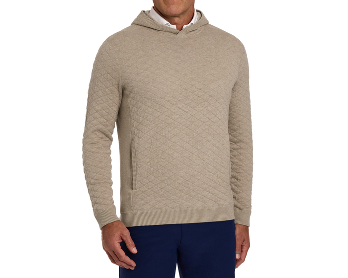 The Wallace Hoodie Sweater: Heathered Light Dune, a light-tan quilted pullover with ribbed cuffs, hem, and side pocket, worn over a white shirt with navy pants.