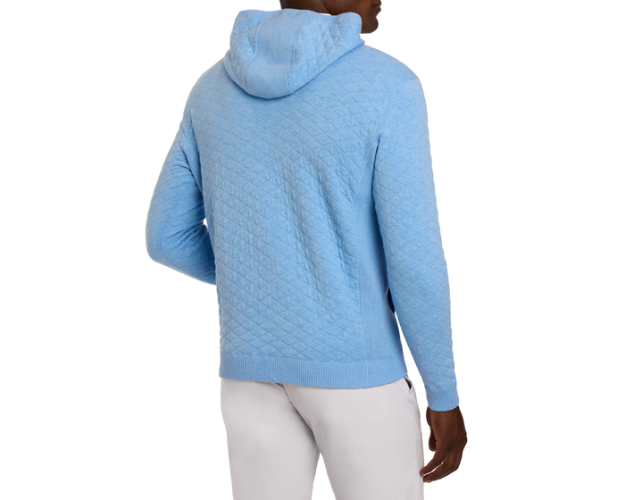 Person wearing The Wallace Hoodie Sweater in Heathered Vista Blue, showcasing a quilted design with ribbed cuffs and hem, paired with light-gray trousers.