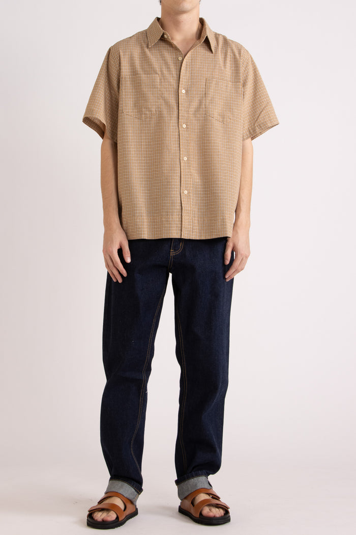 Man wearing a tan checkered shirt, indigo jeans and tobacco slides on a white background