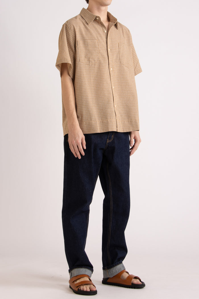 Man wearing a tan checkered shirt, indigo jeans and tobacco slides on a white background
