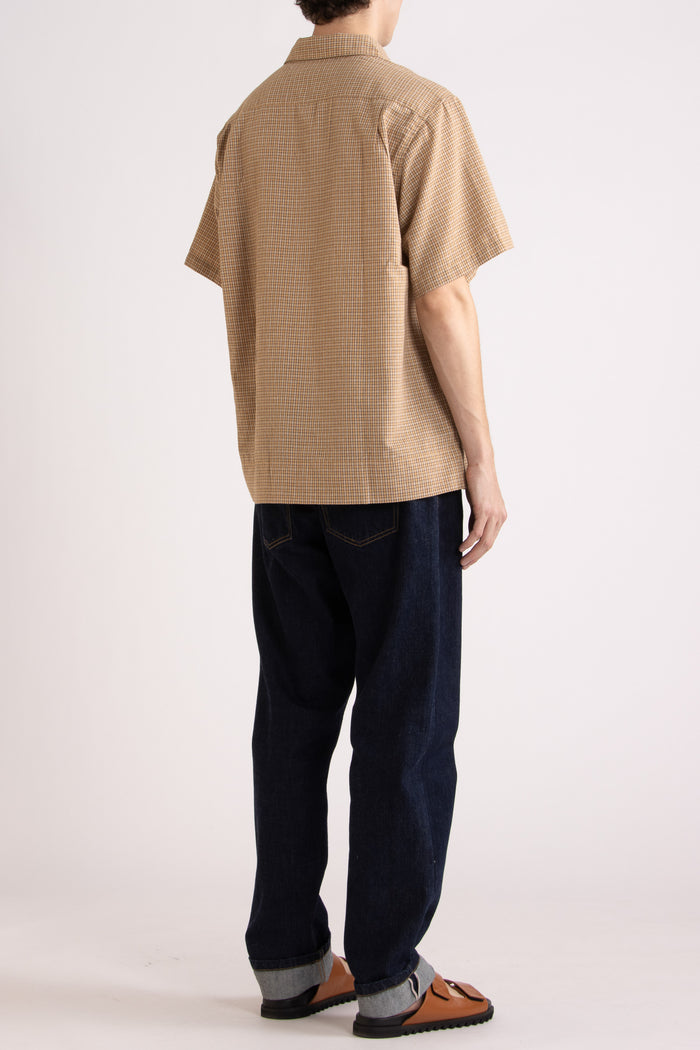 Man wearing a tan checkered shirt, indigo jeans and tobacco slides on a white background