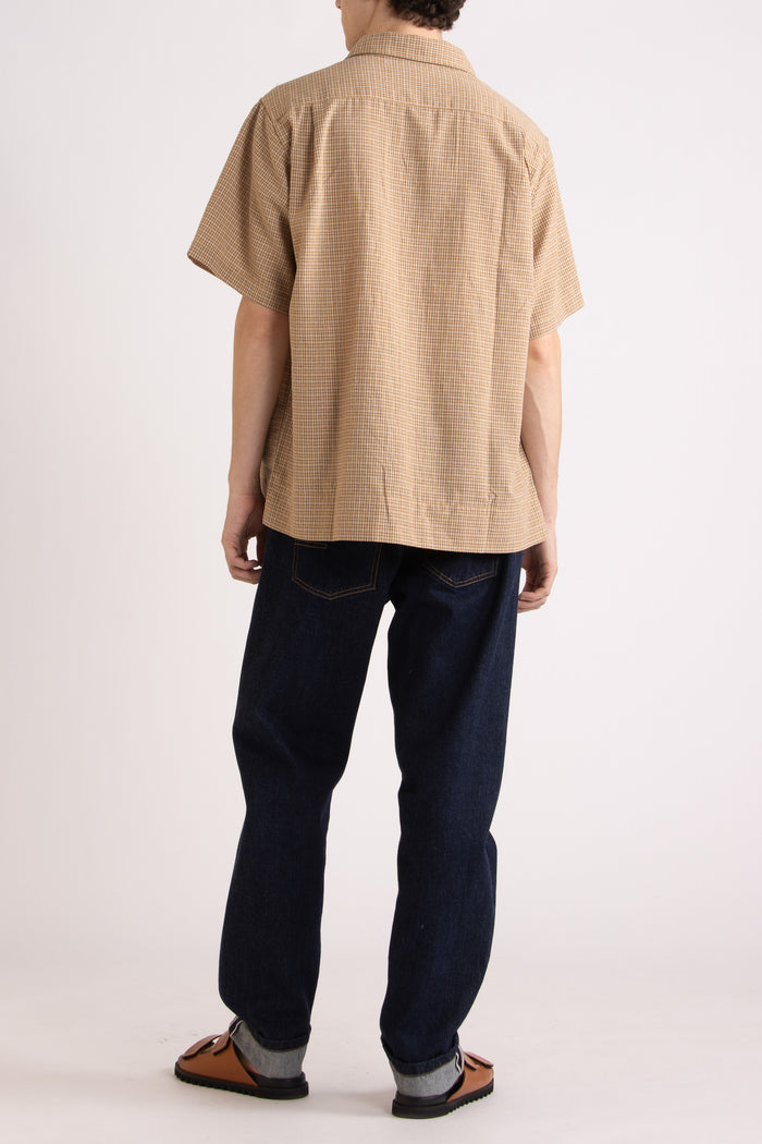 Man wearing a tan checkered shirt, indigo jeans and tobacco slides on a white background
