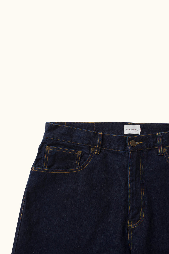 Close up of Indigo Jeans featuring button and stitching detailing on a white background