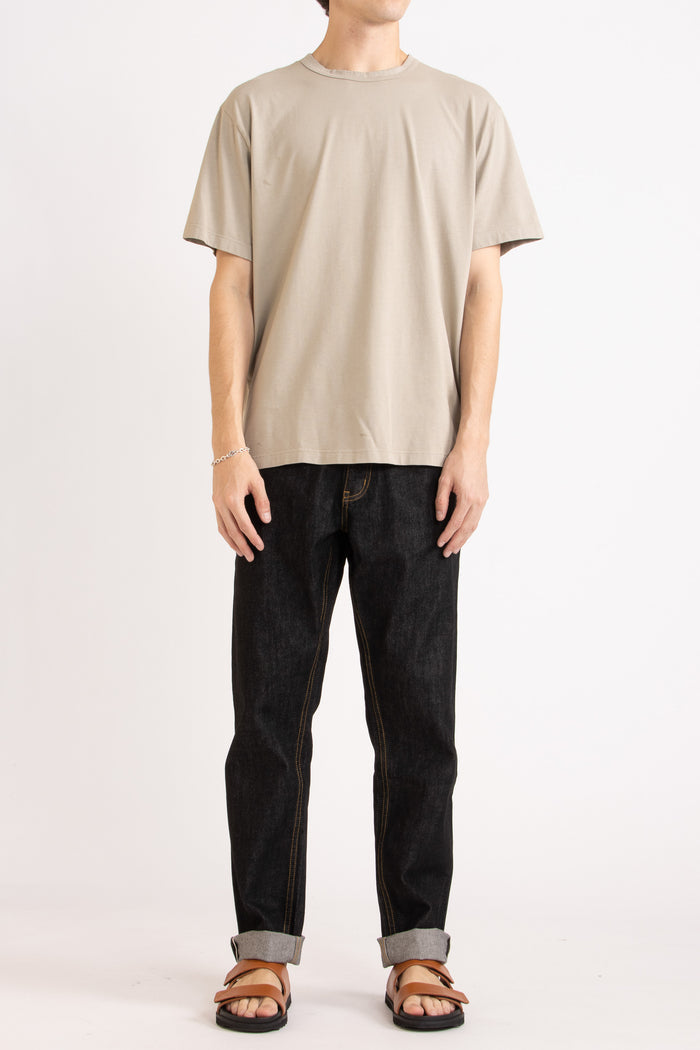 Man wearing a oat t-shirt, black jeans and tobacco slides on a white background