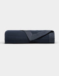 The Cozy Earth Waterfront Grid Matelasse Blanket is neatly folded in dark navy blue, showcasing its smooth, textured surface with one corner turned over, set against a plain light background.|Color:Eclipse