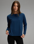 A person with long brown hair is wearing the Cozy Earth Women’s All Day Long Sleeve Tee in navy blue and black pants, standing against a plain gray background and looking at the camera.|Color:Obsidian
