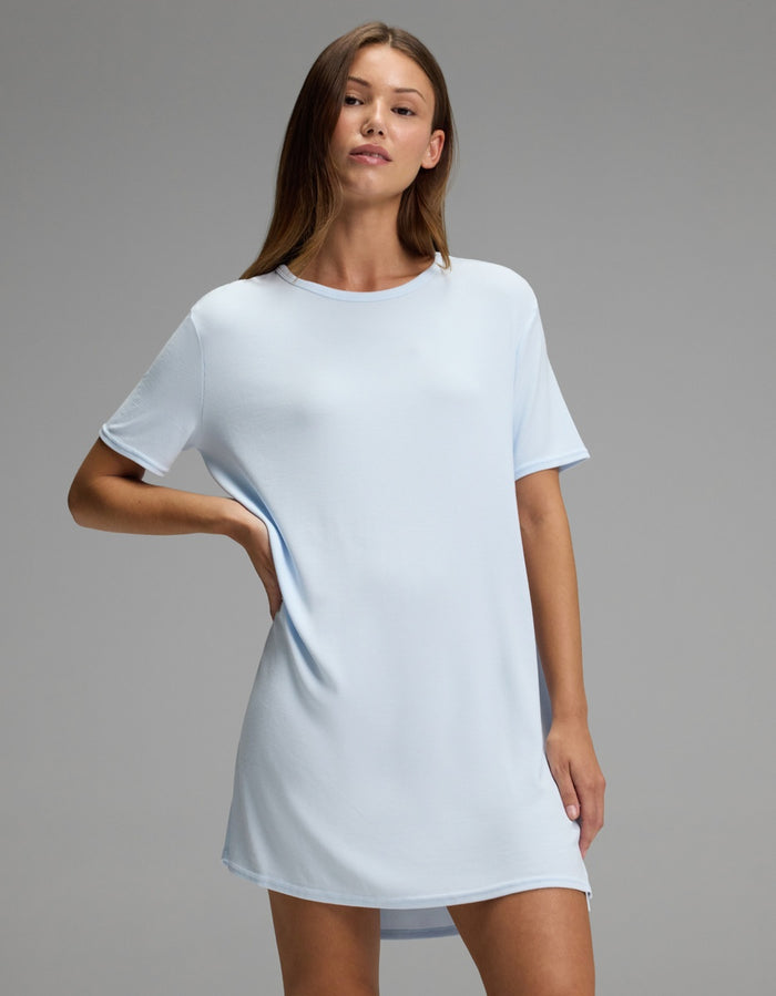 A woman models the Cozy Earth Women’s Bamboo Rib-Knit Boyfriend Sleep Dress in light blue, standing against a plain gray background with one hand on her hip and the other relaxed by her side.|Color:Frost