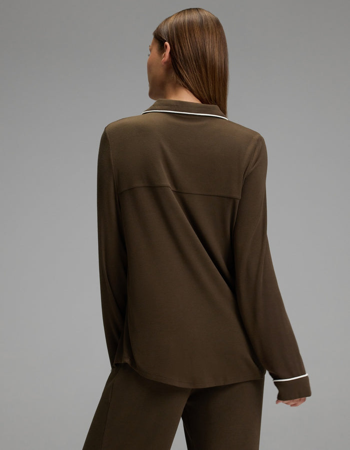 A person with straight brown hair is seen from behind wearing a Cozy Earth Women’s Bamboo Rib-Knit Classic Long Sleeve Pajama Top in brown, featuring white piping along the collar and cuffs, paired with matching pants. The background is plain and gray.|Color:Espresso