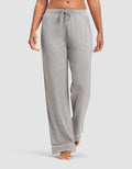 A woman wears Cozy Earth Women's Bamboo Stretch-Knit Pajama Pants in light gray, featuring a drawstring waist and white trim at the cuffs, standing barefoot against a plain background.|Color:Grey