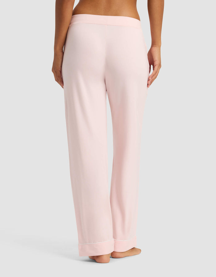 A person is standing barefoot on a neutral background, shown from the back, wearing Cozy Earth Women's Bamboo Stretch-Knit Pajama Pants in light pink with a wide waistband.|Color:Blossom