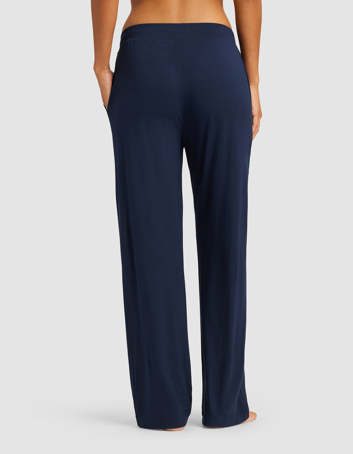 A woman is shown from the waist down, barefoot against a neutral background, wearing Cozy Earth Women's Bamboo Stretch-Knit Pant in navy blue with a relaxed fit and elastic waistband.|Color:Navy