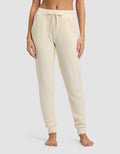 A person wears Cozy Earth's Women's Blake Waffle Jogger in cream, featuring a ribbed knit, drawstring waist, and pockets, while standing barefoot against a plain background.|Color:Coconut