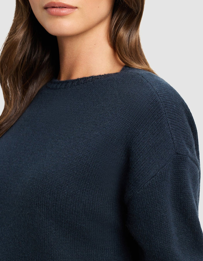 A woman with long brown hair is shown from the shoulders up, wearing the Cozy Earth Women's Brooklyn Sweater Dress in dark blue against a neutral background.|Color:Eclipse