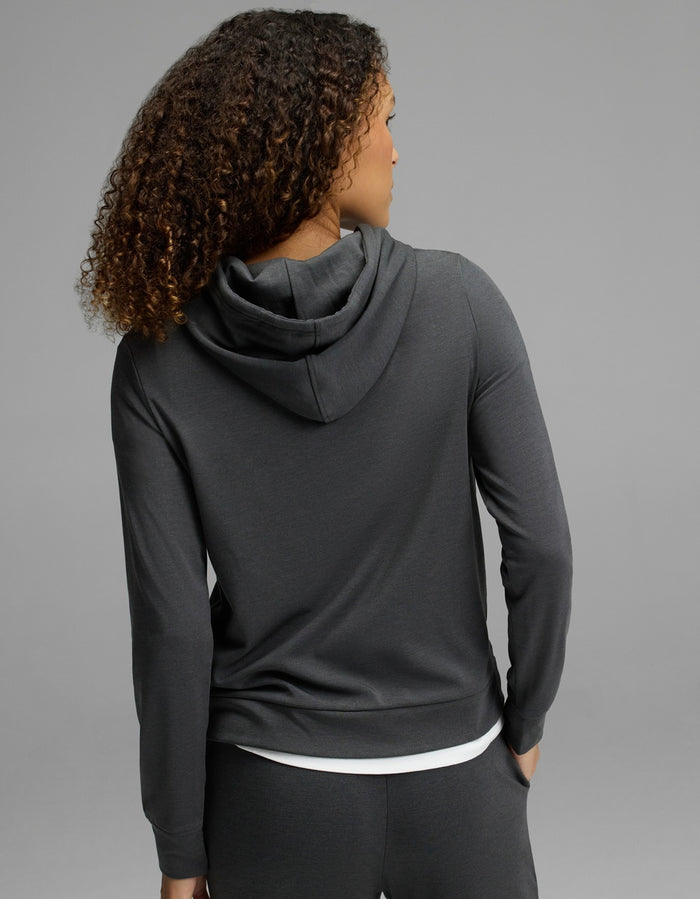 A woman with curly hair is shown from the back, wearing the Cozy Earth Women’s Brushed Bamboo Hoodie in dark gray, against a plain gray background.|Color:Charcoal
