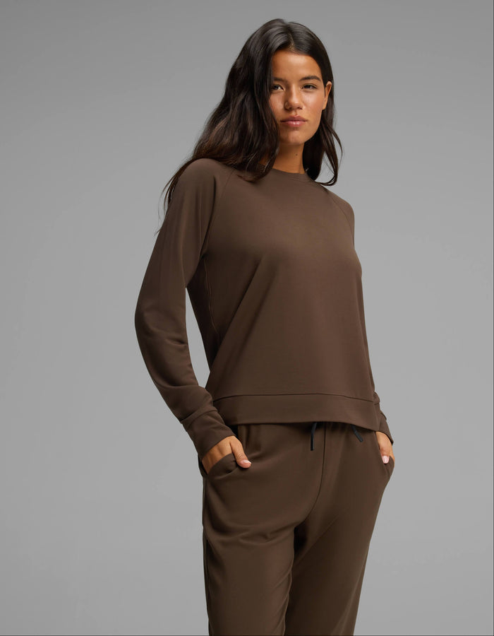A woman with long dark hair stands confidently with one hand in her pocket against a plain light gray background, wearing the Cozy Earth Women's Brushed Bamboo Jogger Set in a matching brown shade.|Color:Espresso