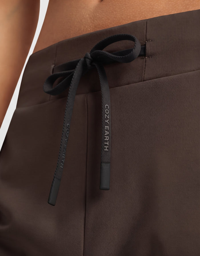 Close-up of a person wearing the Women's Brushed Bamboo Jogger Set by Cozy Earth, featuring brown pants with a black drawstring tied in a bow and "COZY EARTH" printed in white lettering.|Color:Espresso