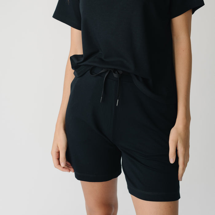 Woman wearing a black t-shirt and black Cozy Earth Brushed Bamboo Mid-Length Shorts shorts on a plain background |Color:Black