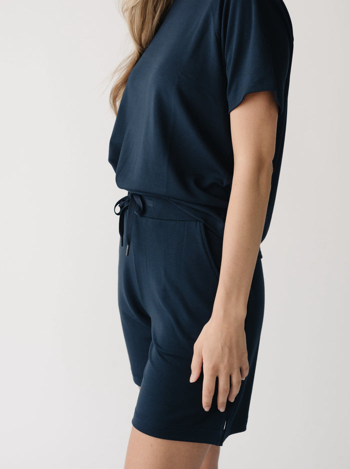 Woman wearing a navy t-shirt and navy Cozy Earth Brushed Bamboo Mid-Length Shorts shorts on a plain background |Color:Navy