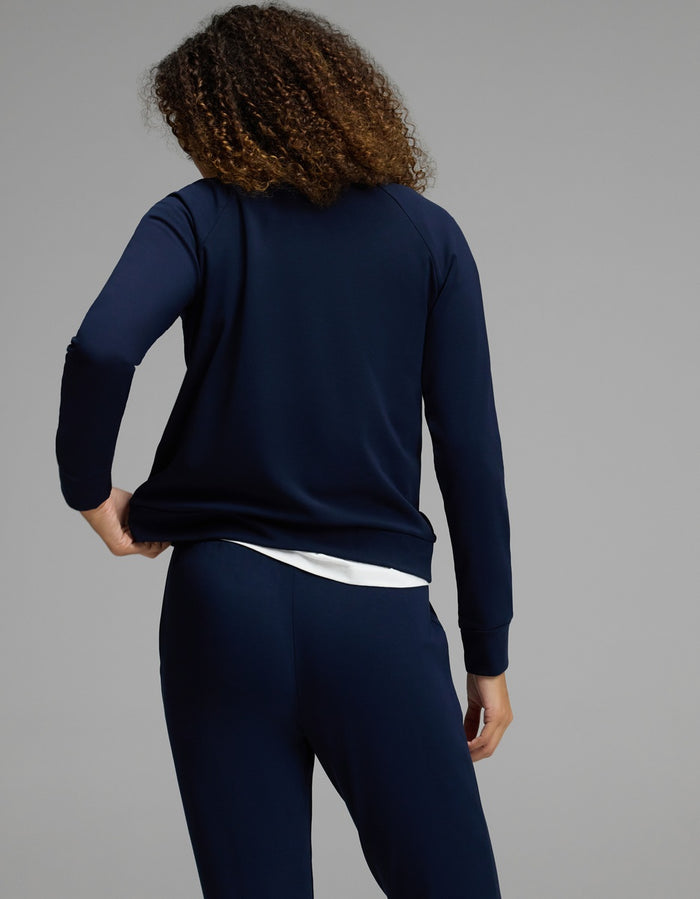 A person with curly hair, seen from behind, wears the Cozy Earth Women’s Brushed Bamboo Mock Neck & Jogger Set in navy over a white shirt, standing against a plain gray background.|Color:Navy