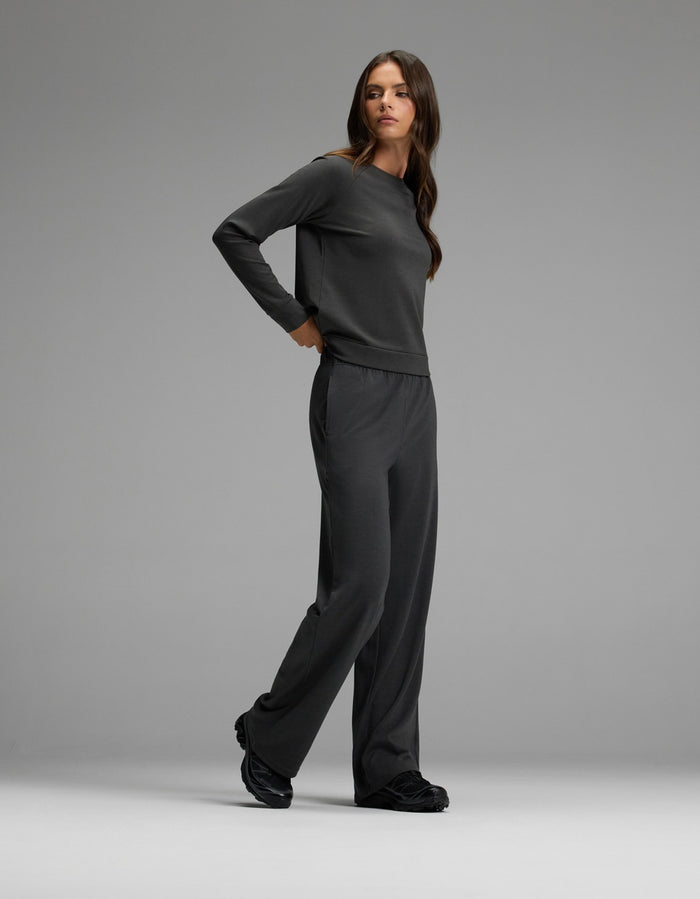 A woman with long brown hair wears the Cozy Earth Women’s Brushed Bamboo Wide Leg Pull On Pant & Pullover Crew Set in dark grey, paired with black shoes, standing against a plain light grey background.|Color:Charcoal