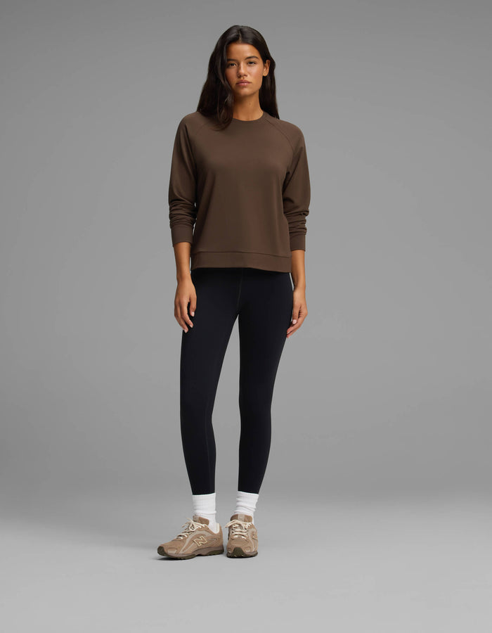 A woman stands against a gray background wearing the Cozy Earth Women's Brushed Bamboo Pullover Crew in brown, paired with black leggings, white socks, and tan sneakers. She looks at the camera with a neutral expression.|Color:Espresso