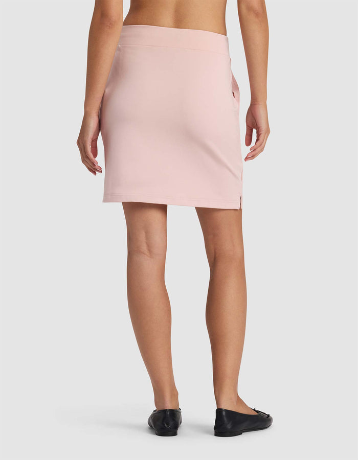 A person is seen from behind wearing Cozy Earth's Women's Brushed Bamboo Skirt in light pink with black flats, set against a plain white background.|Color:Dusty Rose