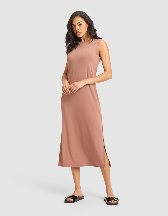 A woman models the Cozy Earth Women's Brushed Bamboo Sleeveless Midi Dress in light brown, paired with black slide sandals featuring gold accents, posing against a plain light gray background. |Color:Saddle
