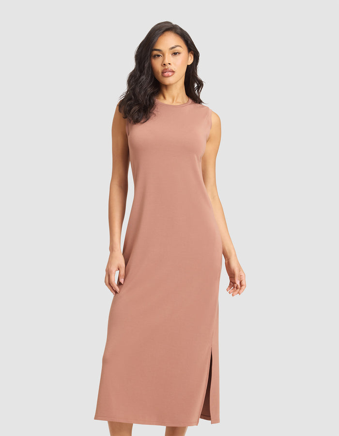 A woman models the Cozy Earth Women's Brushed Bamboo Sleeveless Midi Dress in dusty pink, featuring a side slit, against a plain light gray background. |Color:Saddle