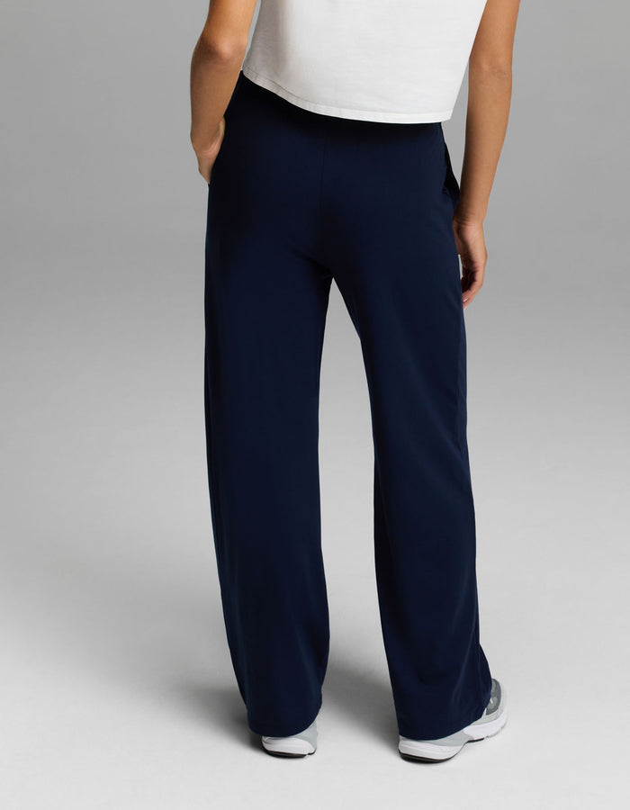 A person stands with their back to the camera against a plain grey background, wearing a white short-sleeve top, white sneakers, and the Cozy Earth Women’s Brushed Bamboo Wide Leg Pull-On Pant in dark blue.|Color:Navy