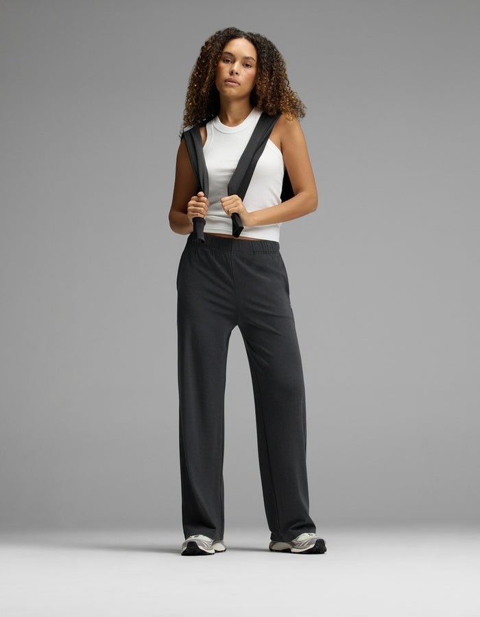 A person with curly hair wears a white sleeveless top and Cozy Earth’s Women’s Brushed Bamboo Wide Leg Pull-On Pant, standing confidently against a plain gray background.|Color:Charcoal