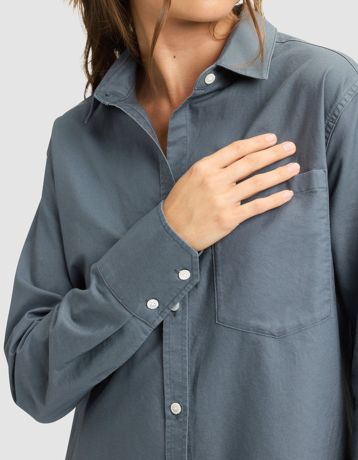 A woman wearing the Cozy Earth Women's Camden Dress touches the chest pocket with her right hand. Her face is partially out of frame, and the background is plain light gray. |Color:Dawn