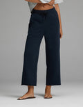 A person is wearing the Cozy Earth Women’s Chelsea Cropped Pant in Eclipse, featuring a drawstring waist and wide-leg silhouette, paired with a light gray cropped top and brown sandals. Only the lower torso and legs are visible, standing against a plain gray background.|Color:Eclipse