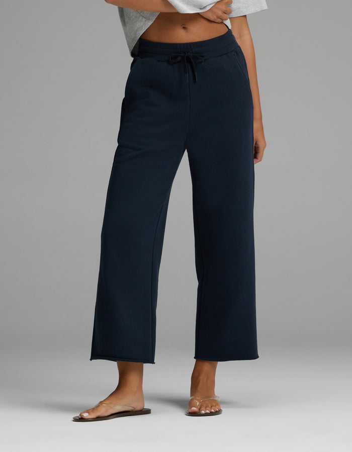 A person is wearing the Cozy Earth Women’s Chelsea Cropped Pant in Eclipse, featuring a drawstring waist and wide-leg silhouette, paired with a light gray cropped top and brown sandals. Only the lower torso and legs are visible, standing against a plain gray background.|Color:Eclipse