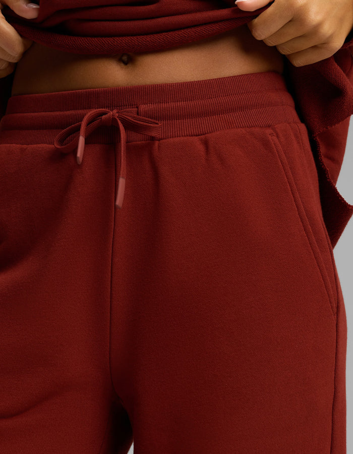 Close-up of a person wearing Cozy Earth’s Women's Chelsea Set, featuring high-waisted, drawstring maroon sweatpants and a matching maroon top, lifted to reveal part of their midriff and belly button.|Color:Currant