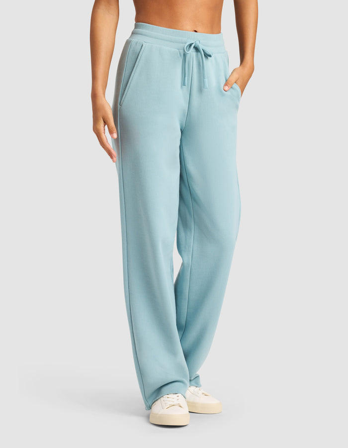 A person models the Cozy Earth Chelsea Pant in light blue with pockets and drawstring, paired with off-white sneakers, standing against a plain light background. The upper body is partially out of frame.|Color:River
