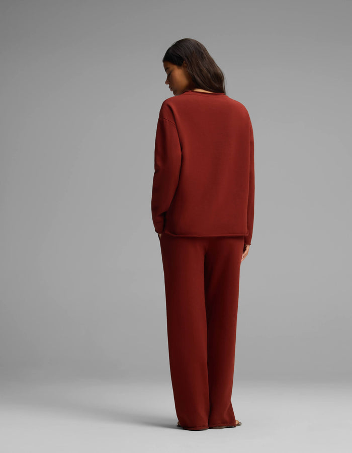 A person with long dark hair stands facing away, wearing the Cozy Earth Women's Chelsea Set—a loose-fitting, long-sleeve dark red top and matching wide-leg pants—against a plain gray background.|Color:Currant